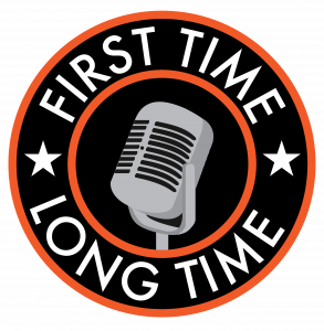 A two leveled circle with an old fashioned microphone in the smaller circle. Around the edges it reads "First Time Long Time". There are small white stars on the right and left sides of the circle.
