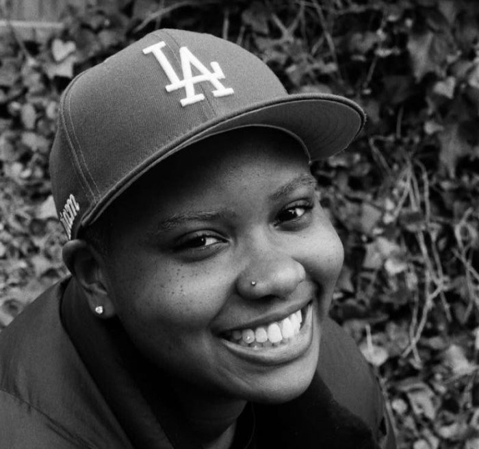 Liam Archer, wearing a baseball cap, smiles upwards in a black and white photo.