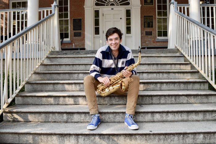 Photo of Ben Telerski sitting on the steps of Old North and holding a saxophone