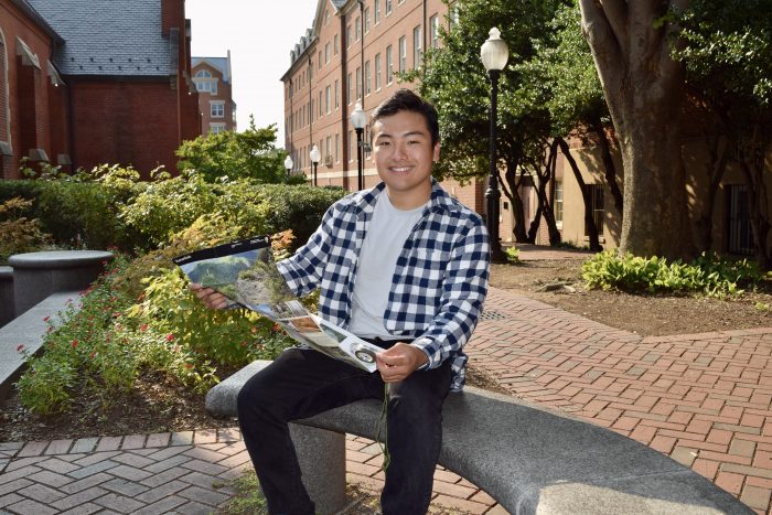 Photo of Harrison Lee holding a map and sitting on a bench in Dahlgren Quad.