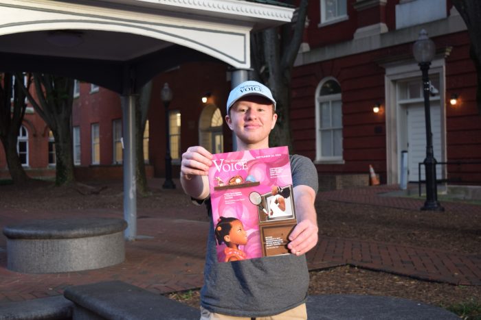 Photo of Ethan Greer wearing a blue "The Georgetown Voice" cap and holding out the latest issue in Dahlgren Quad
