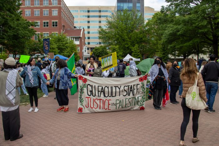 Faculty and staff holding hands to form a human chain. In the center, two faculty members are holding a banner which reads, "GU Faculty & Staff for Justice in Palestine."