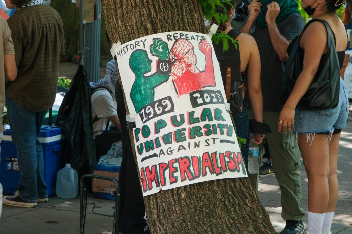 A sign taped to a tree, which reads, "Popular University Against Imperialism."