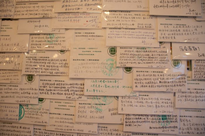 Postcards on the wall of JF books. The postcards are written in Chinese, and they are collaged on top of each other.