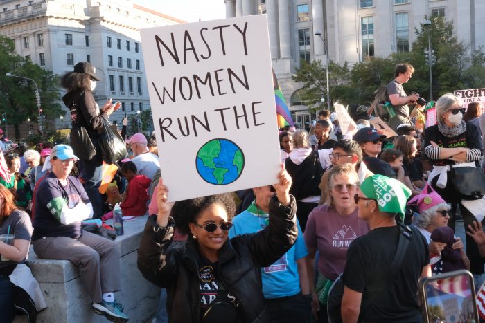 A protester carries a sign that reads, "Nasty women run the," with a drawing of Earth at the bottom.