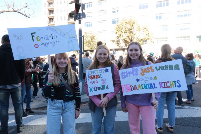 Three young girls stand together holding signs that read “Femininomenon,” “Regulate Guns Not Women,” and “Girls Just Wanna Have FUNdamental Rights”