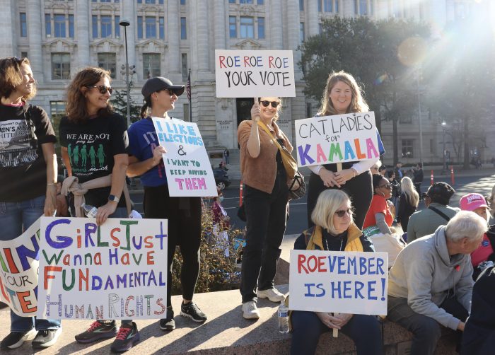 A group of protesters at the Women's March carry signs urging people to vote. The signs read, "Roe Roe Roe your vote," "Cat ladies for Kamala," "I like elections and want to keep having them," and "Roevember is here."