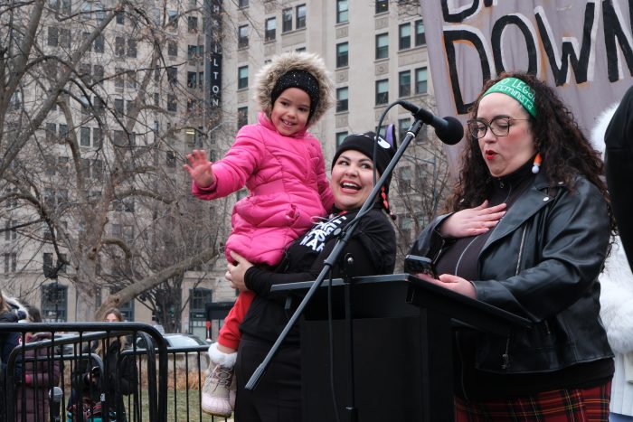 A woman holds up a little girl wearing a pink coat, who waves at the crowd while McGuire speaks at the podium