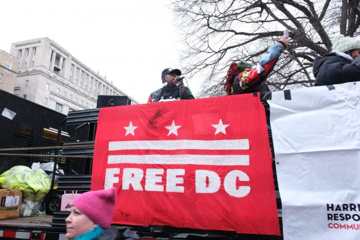 Organizers with Harriet’s Wildest Dreams stand and speak on top of a truck with a red flag draped over the side reading ‘Free D.C.’