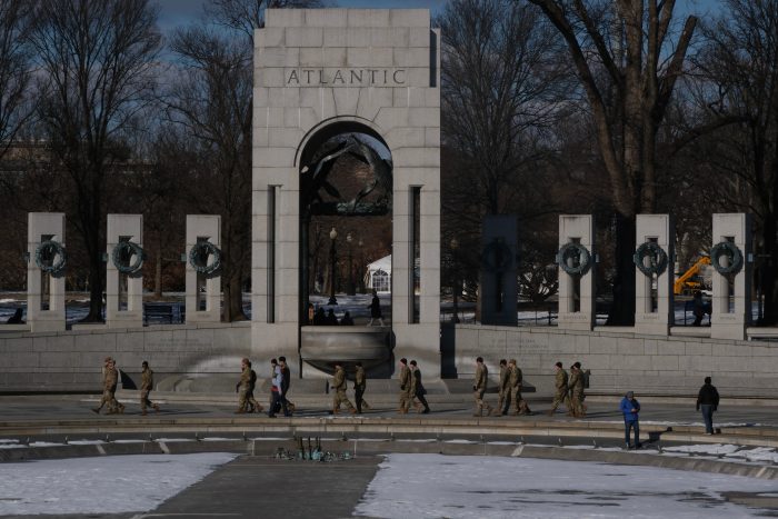 A group of people in camouflage walk along the WWII Memorial. The fountain is iced over.