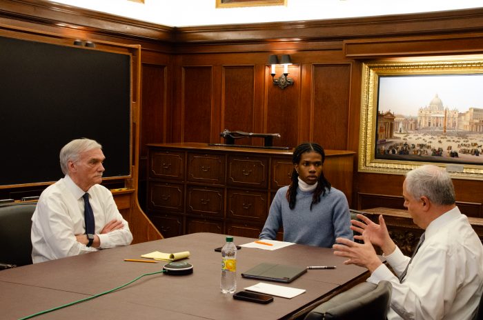 From left to right, Groves, Jones, and Ferrera sit around a table, talking.