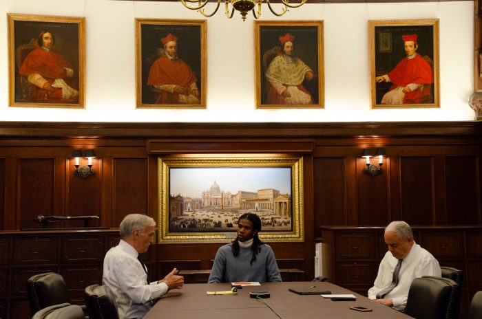 From left to right, Groves, Jones, and Ferrera sit around a table, talking.