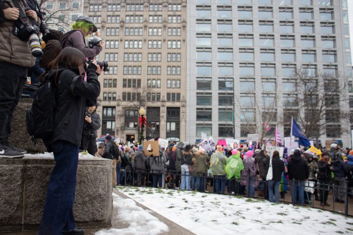 Photographers take photos of a crowd holding several flags and signs