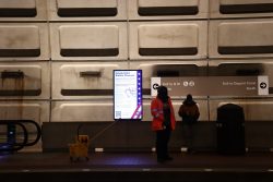 A screen in DuPont Circle Metro Station reads "Inauguration Station Closures." A utilities worker in an orange vest stands in the frame. Photo by Chih-Rong Kuo.