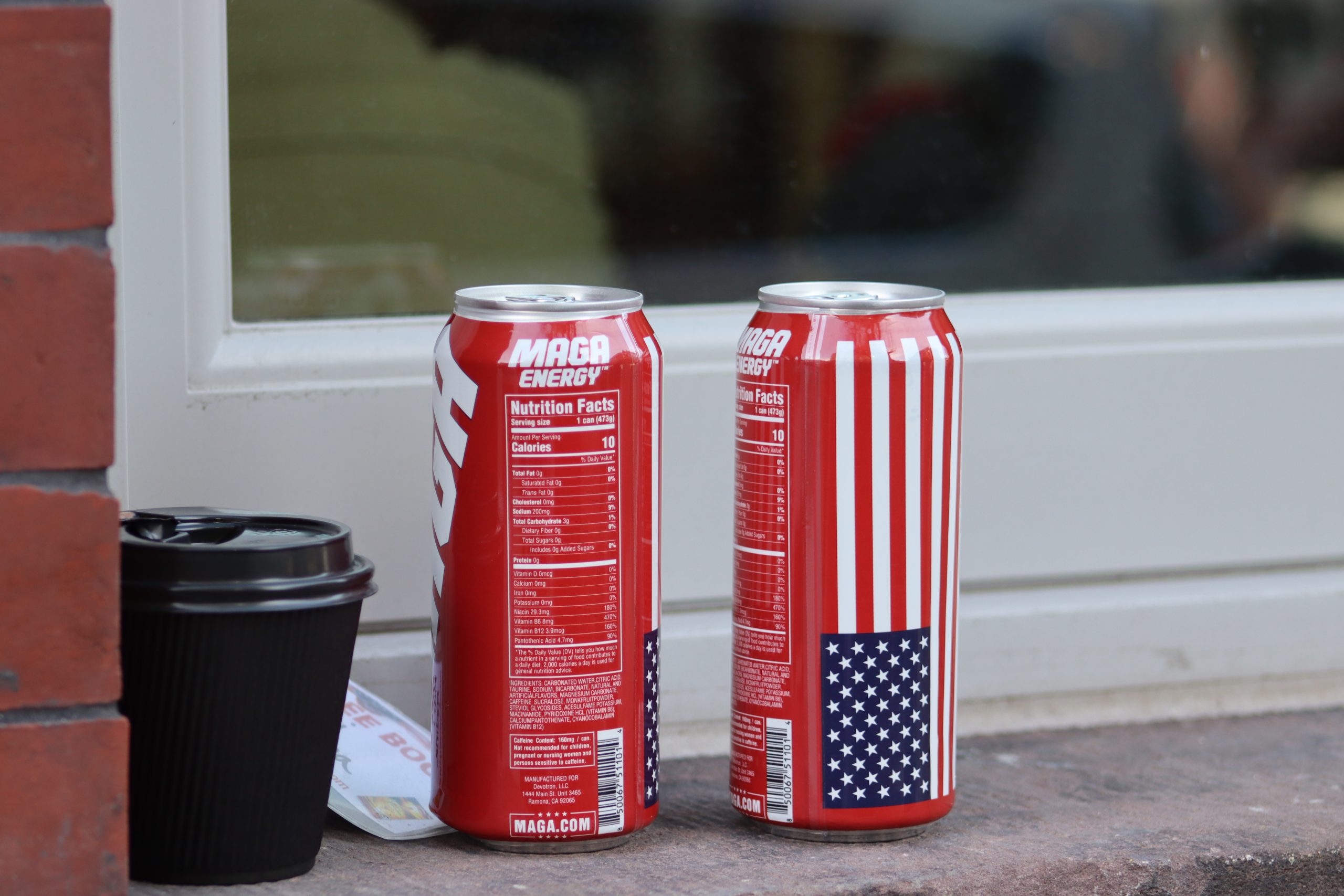 Two red cans of energy drinks sit on a ledge. The cans have American flags and "MAGA ENERGY" printed on them.