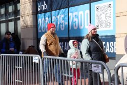 Two parents and their child stand in line, behind a metal barricade. Photo by Chih-Rong Kuo.