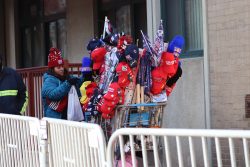 A person pushes a cart overflowing with Trump merch, including flags, MAGA hats, and pins. Photo by Chih-Rong Kuo.