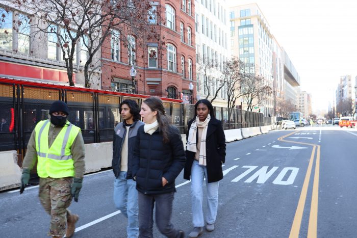 A group of people walks down an empty street, toward the camera.