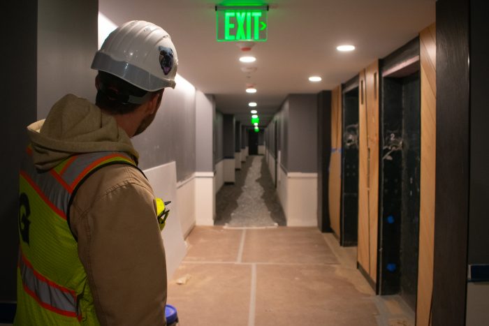 The back of a man, in construction gear, looking down a hallway with mild construction.