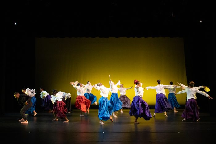 A large group of dancers, divided into three groups, take the floor in differing heights.