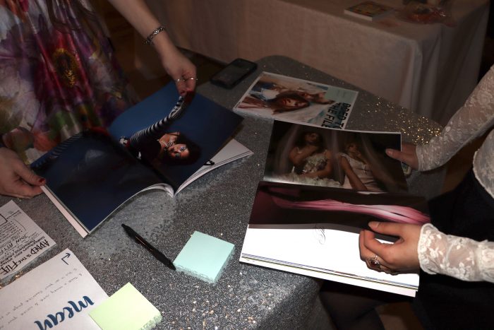 On a table, three copies of a magazine sit while people look through tem