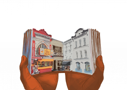 A pair of hands hold open a book. On each open page is a street, with the left side showing a chili bowl restaurant and a hair salon, while the right side shows two white townhouses.