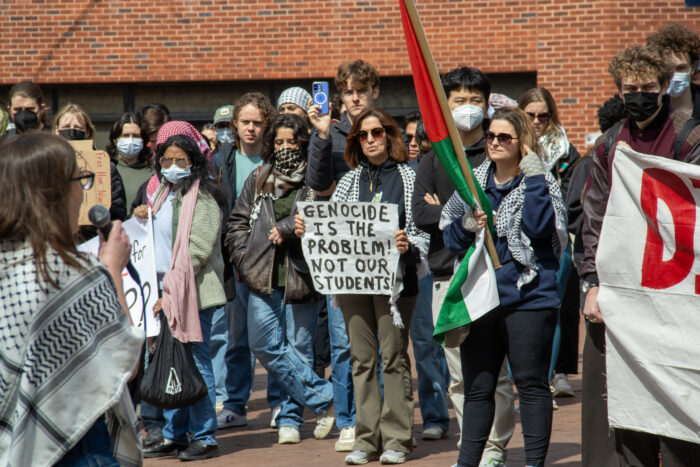 A crowd of protesters stand in red square. A protester in the center carries a sign that reads, "Genocide is the problem, not our students."