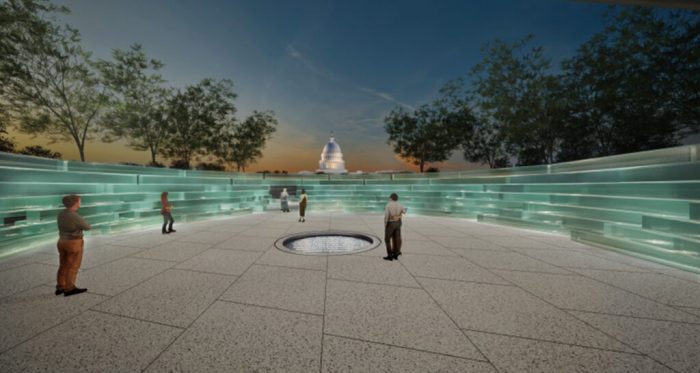 Glass rectangles are arranged in a circular formation. Visitors admire the memorial. The background is dark, showing the Capitol and an orange and blue sky at dusk.