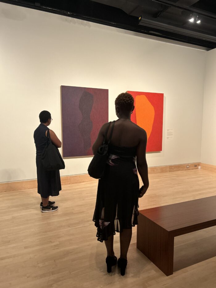 A woman admires artwork aside another person in the gallery.