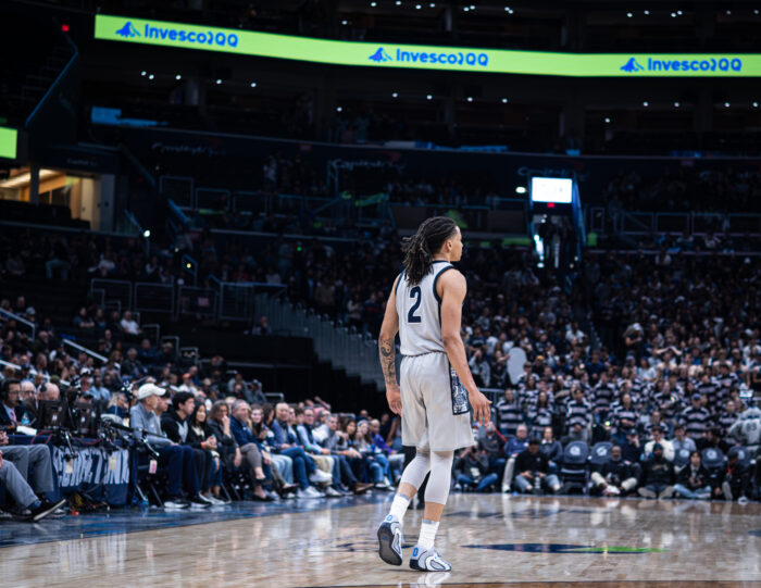 Malik Mack, wearing a grey Georgetown jersey, stands alone in Capital One Arena on the basketball court.