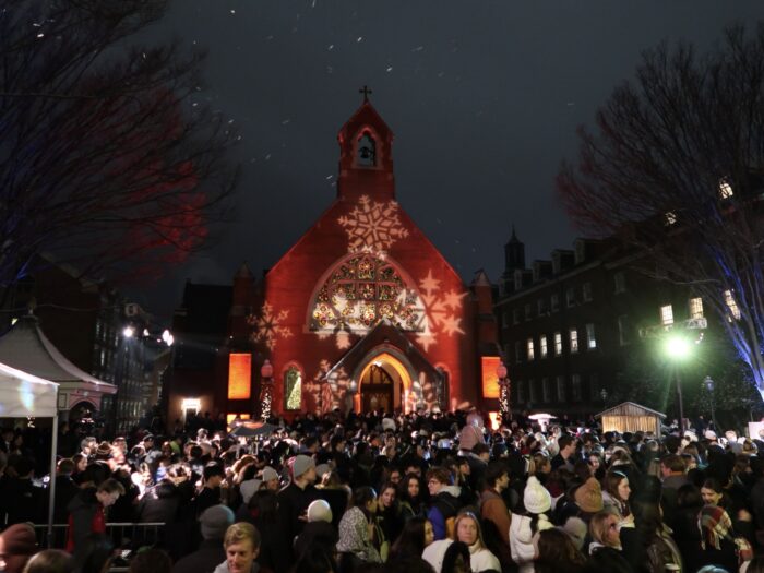 Dahlgren Chapel with snowflakes illuminated on the front, surrounded by a crowd of people.