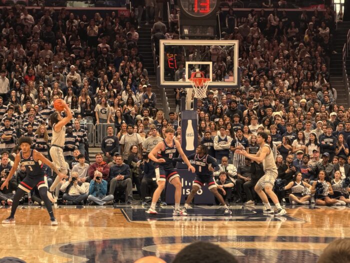 The image shows a Georgetown player shooting a basketball in front of a packed arena.