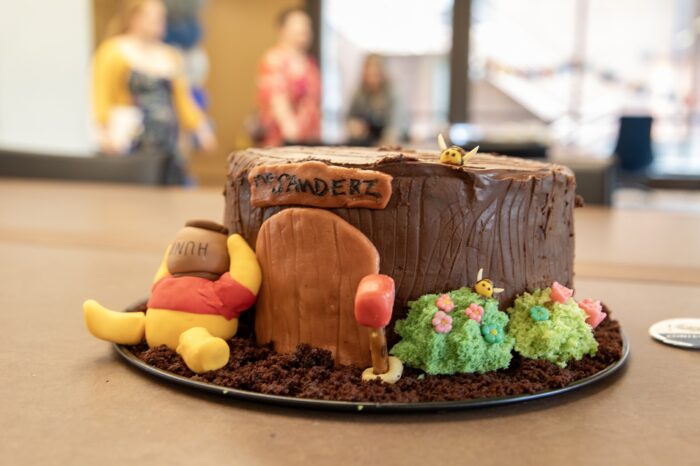 A log-looking Winnie the Pooh-inspired cake sits on a brown table.