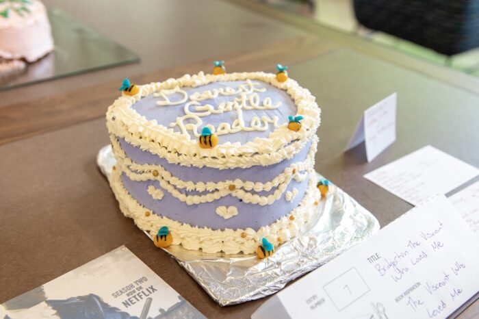 A purple, heart-shaped cake with lettering sits on a brown table.