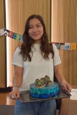 A girl with brown hair proudly holds her blue lagoon-esque cake.