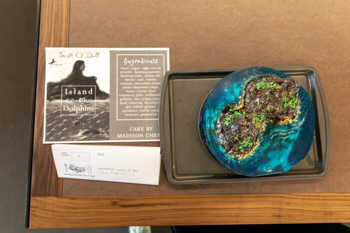 A blue lagoon-esque cake, next to the inspiration material on a brown table.